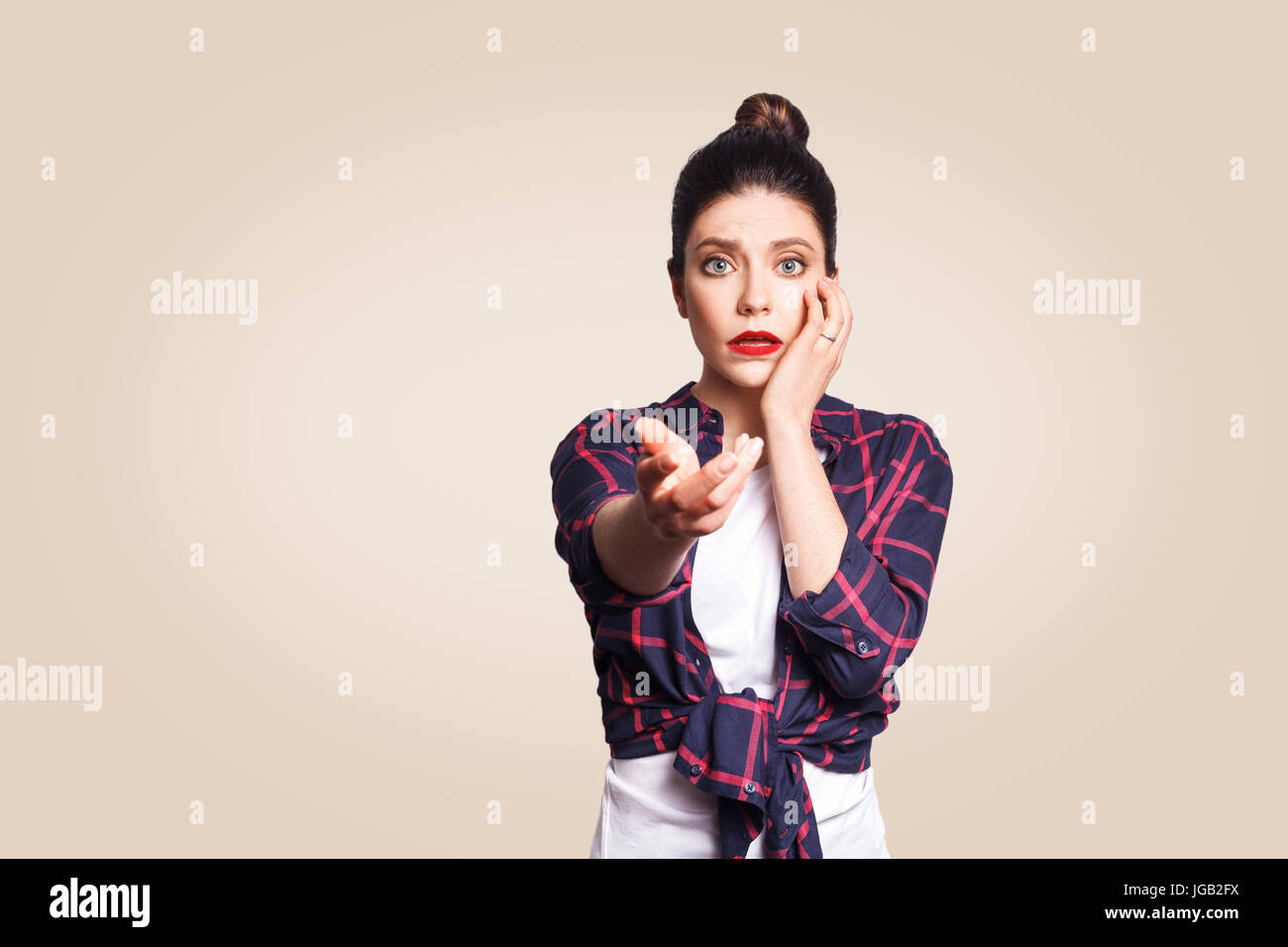 Scared girl with bun hair knot having scared and frightened look, keeping mouth open, touching face and pointing hand at camera. Stock Photo