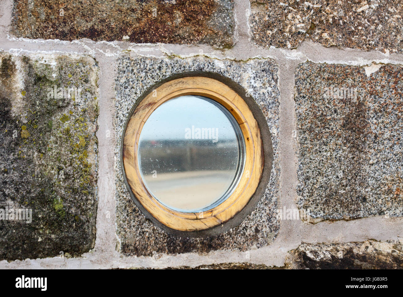 Mirrored, circular porthole window set into cornish granite stone wall. Stock Photo