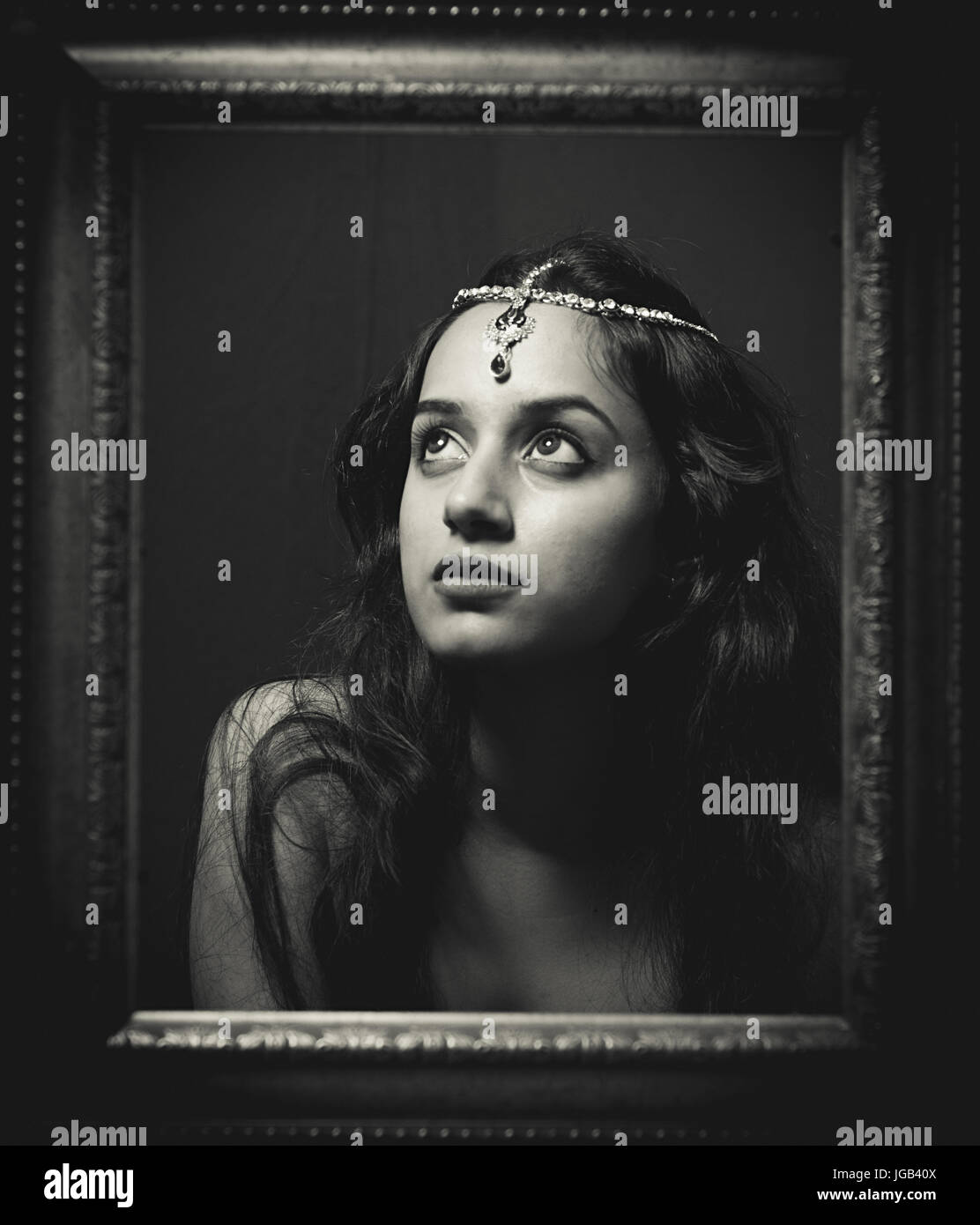 concept traditional shoot with an Indian model wearing a jewellery head piece with gold chain gold shot inside a wooden frame at a studio Stock Photo