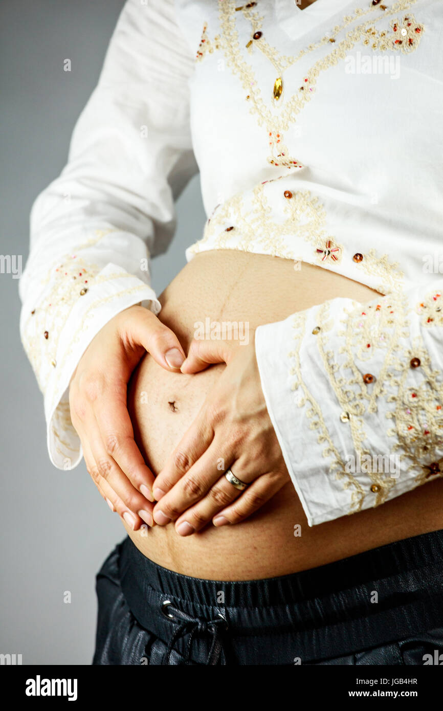 Pregnant woman creating heart shape with her hand on the belly Stock Photo