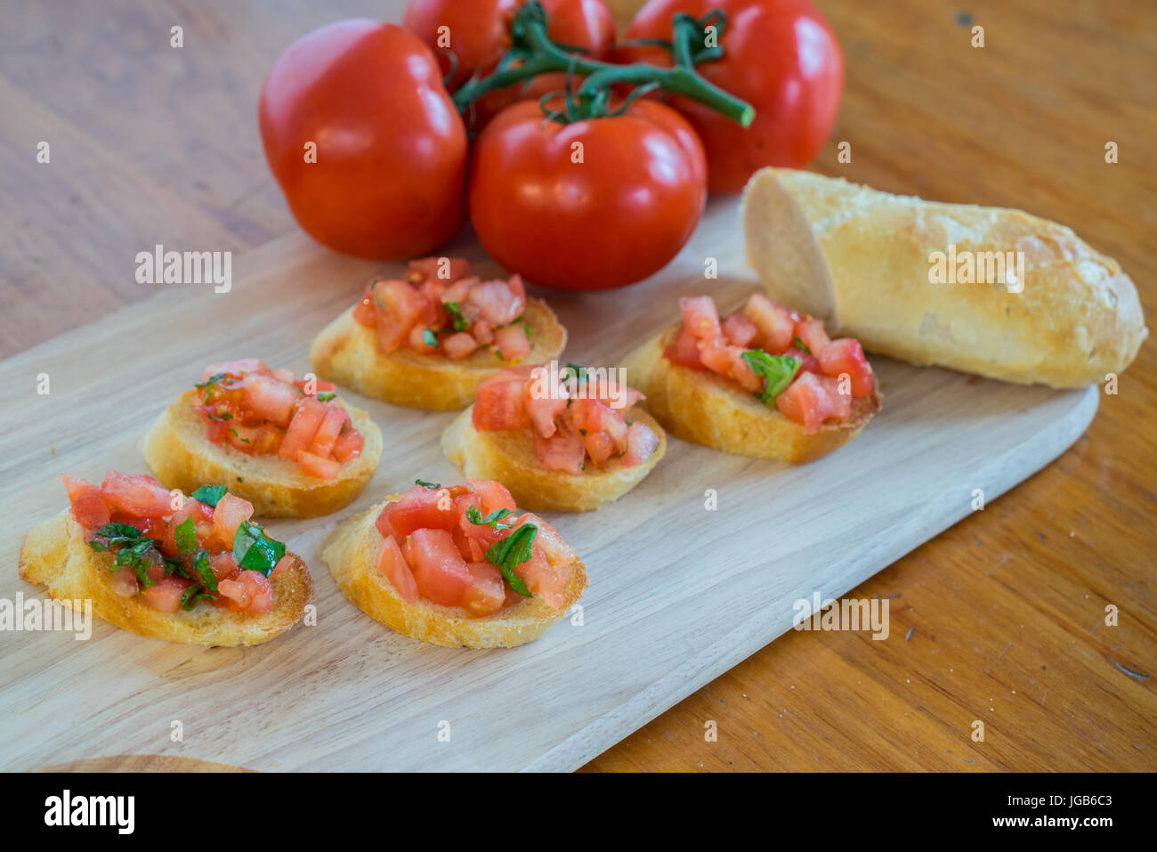 Tomato & basil bruschetta on a wooden cutting board with tomatos and baguette. Stock Photo