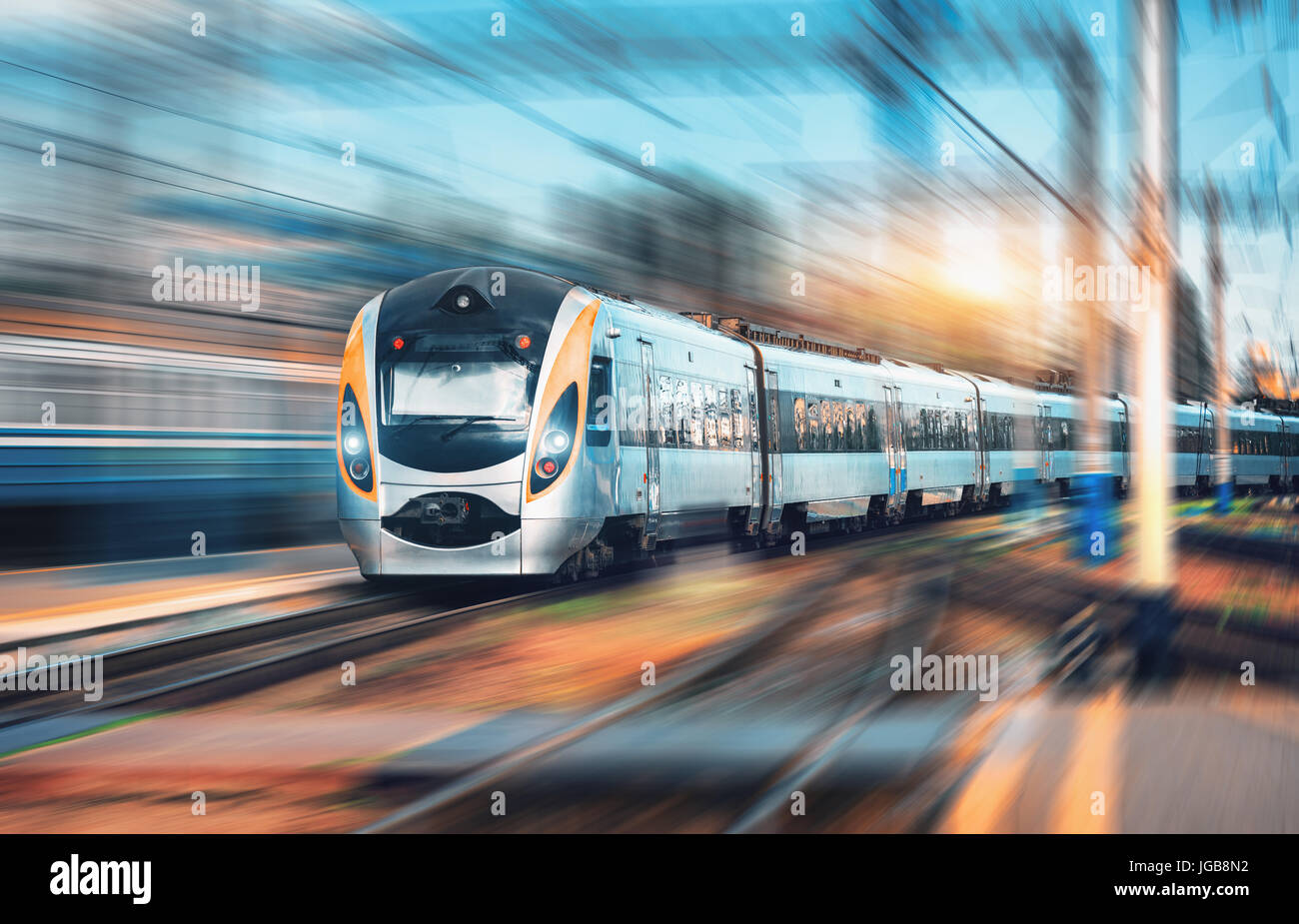 High speed commuter train at the railway station at sunset in Europe. Modern intercity train on railway platform. Urban view with beautiful passenger  Stock Photo