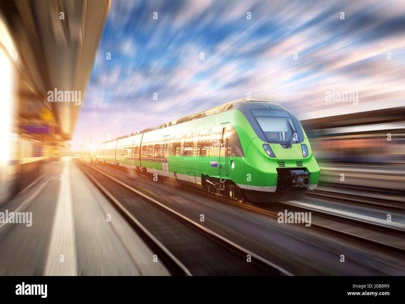 High speed train in motion at the railway station at sunset in Europe. Beautiful green modern train on the railway platform with motion blur effect. I Stock Photo