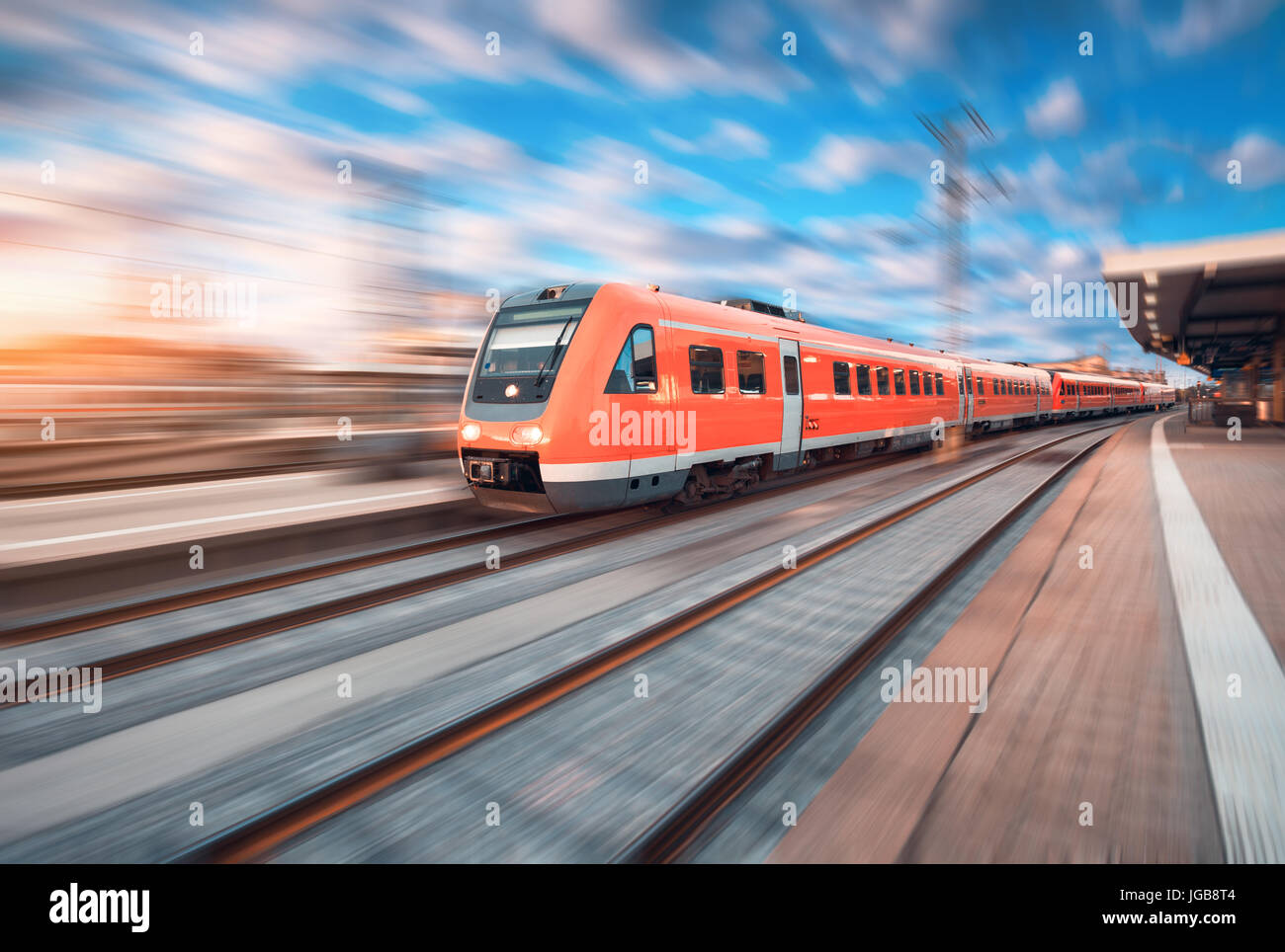 High speed commuter train in motion at the railway station at sunset in Europe. Beautiful red modern train on the railway platform with motion blur ef Stock Photo