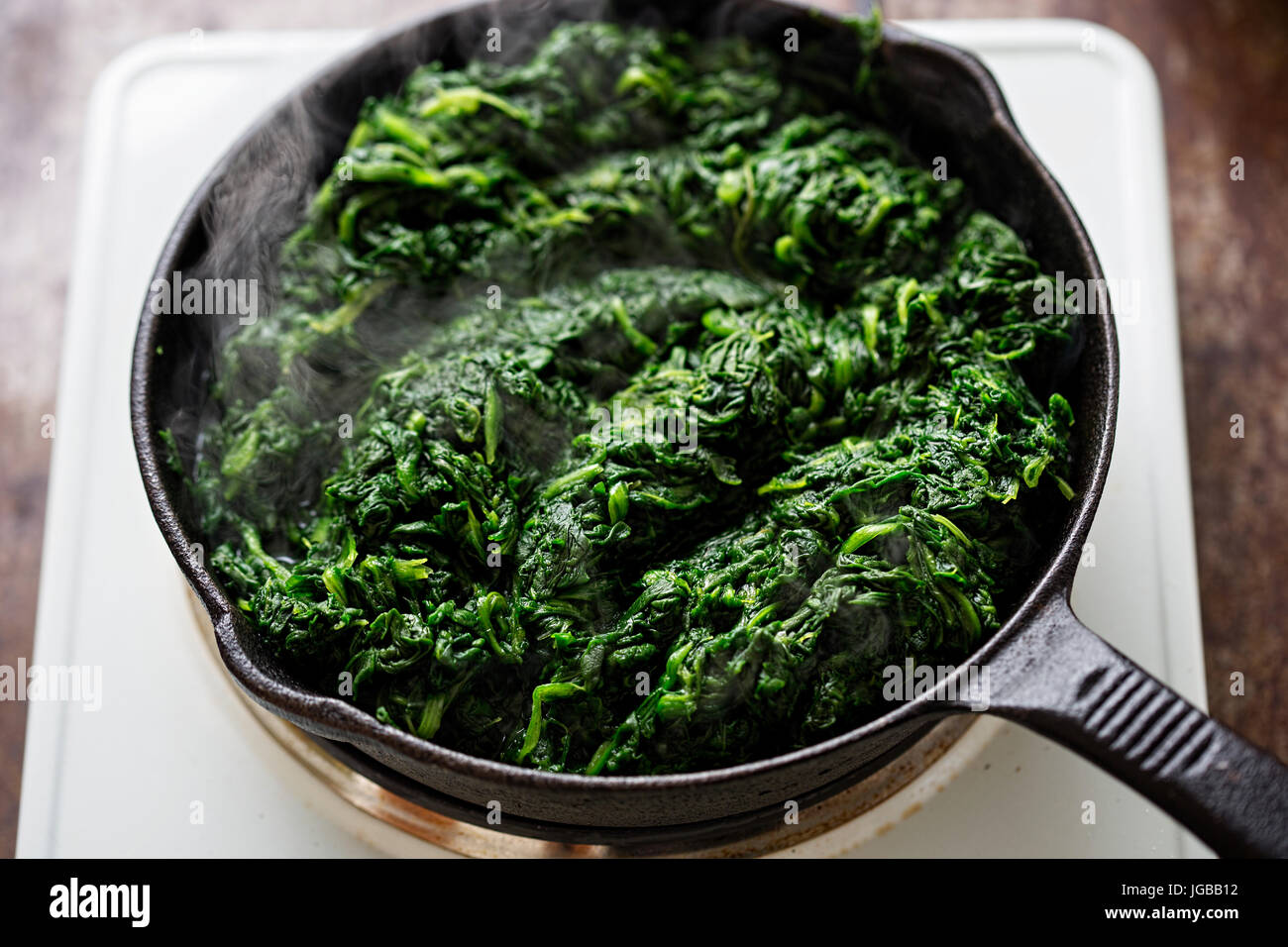 Frying thawed frozen spinach on iron skillet Stock Photo - Alamy