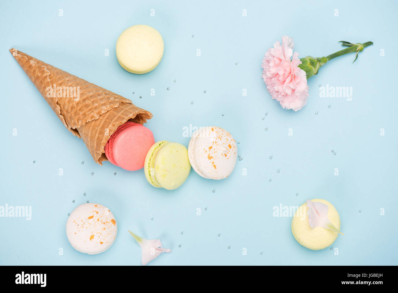 Top view of sweet macarons in waffle cone with pink Carnation. Colorful sweets background Stock Photo