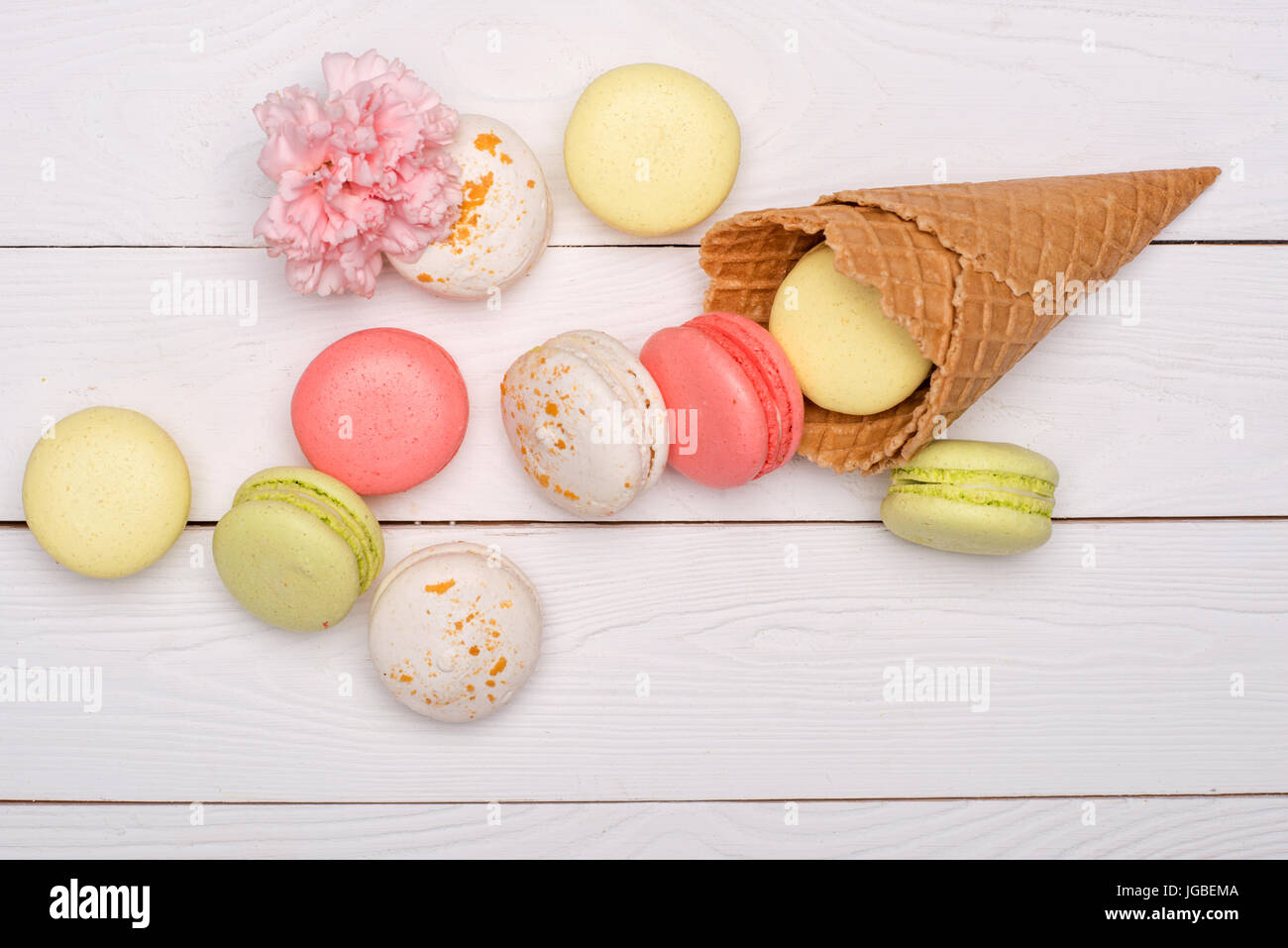 Stack of sweet macaroons and waffle cones styling with flower on wooden surface. sweets background Stock Photo