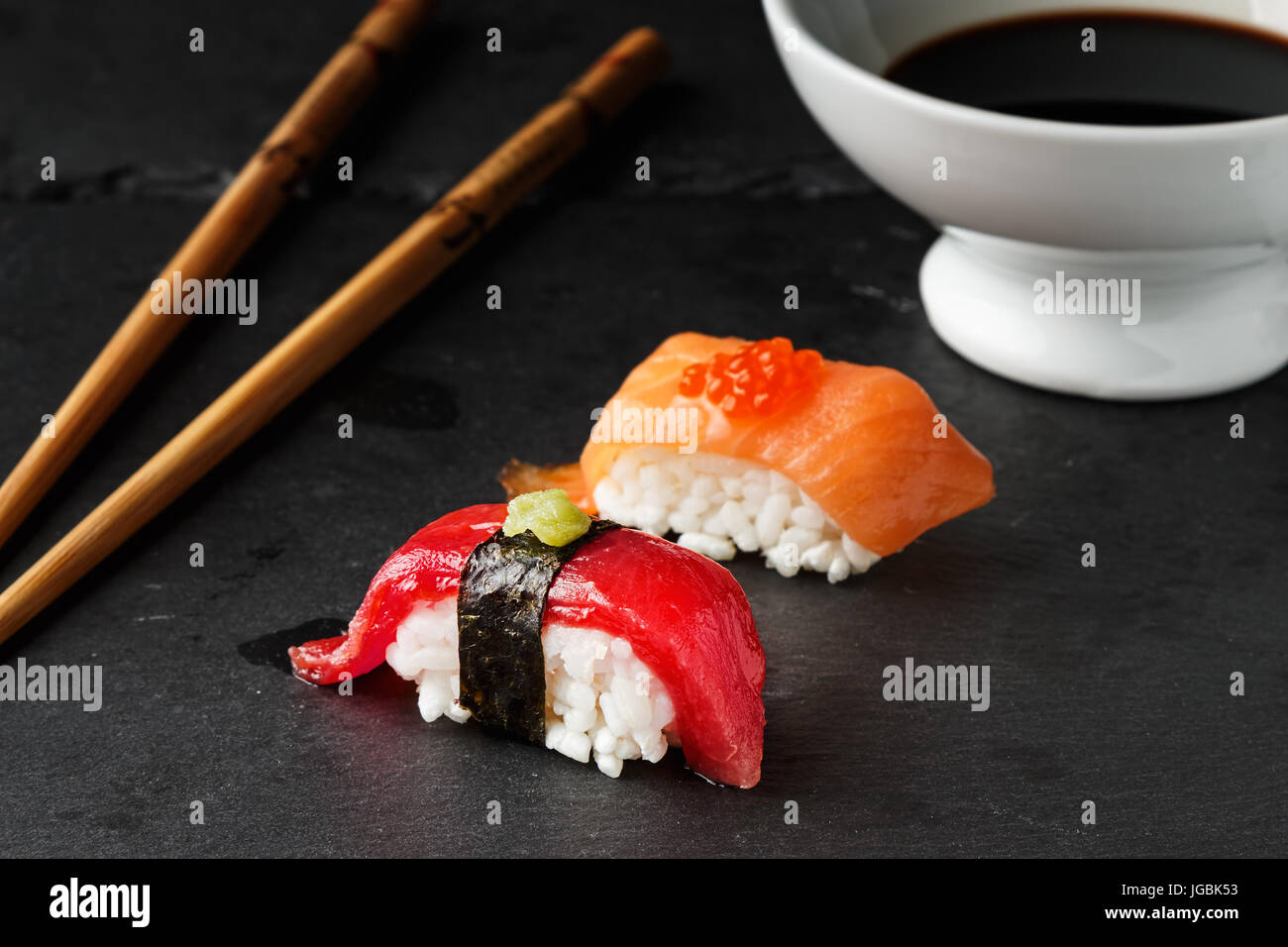 Red tuna Nigiri with Nori seaweed and wasabi paste on black slate stone with chopsticks and bowl of soy sauce. Raw fish in traditional Japanese sushi  Stock Photo