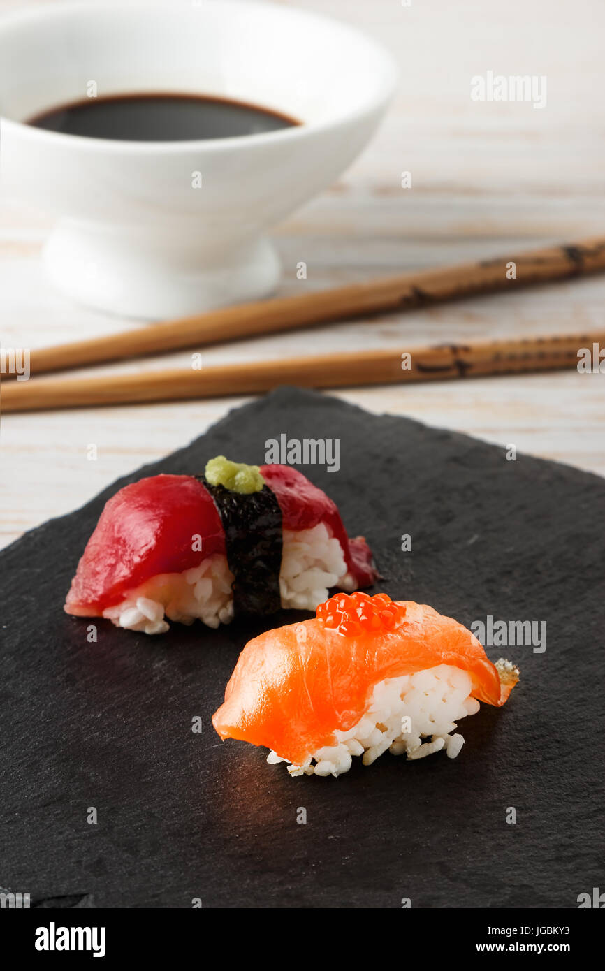 Salmon Nigiri with salmon roe on black slate stone with chopsticks and bowl of soy sauce. Raw fish in traditional Japanese sushi style. Vertical image Stock Photo