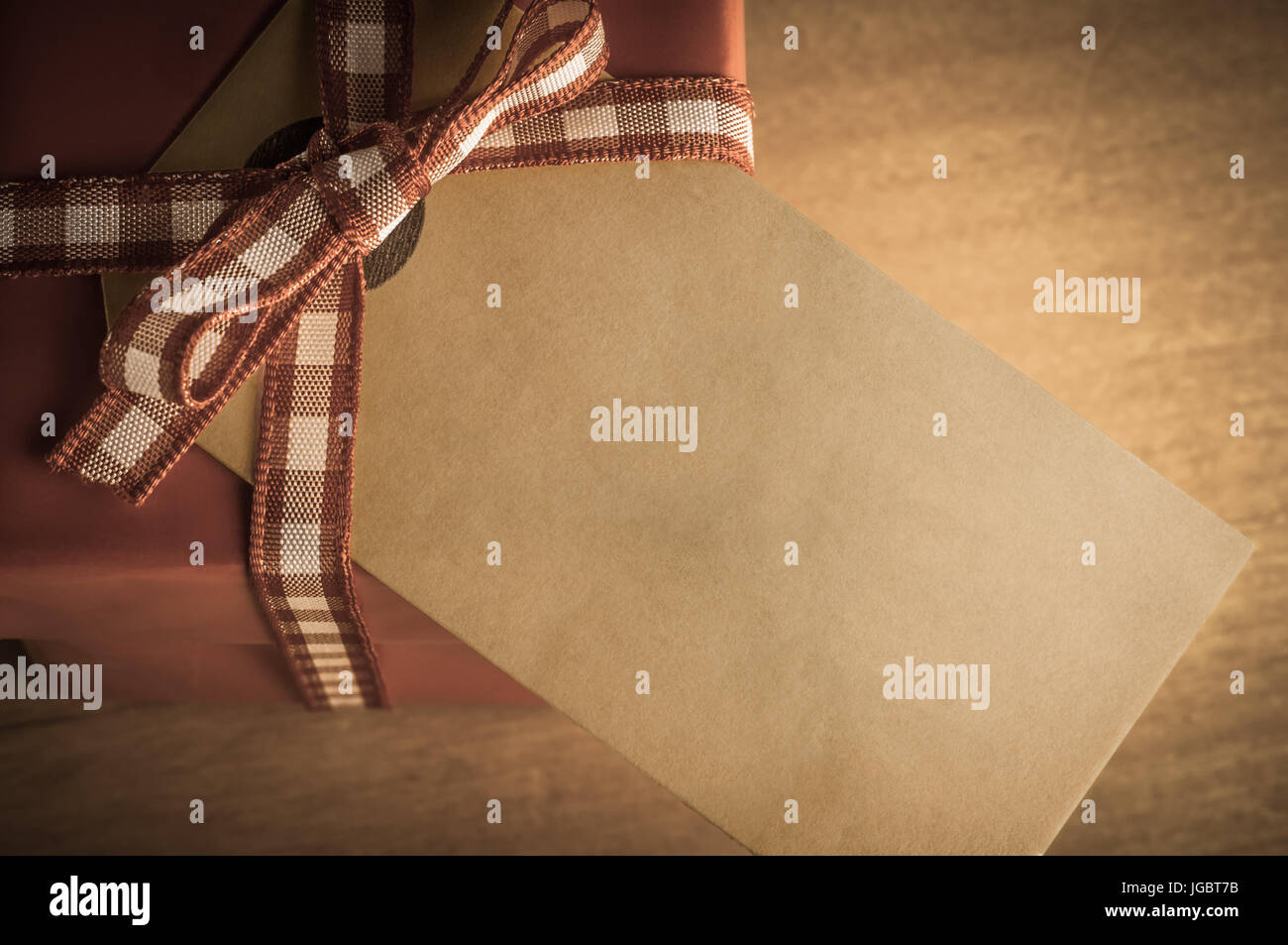 Overhead view of a red Christmas gift box, tied to a bow with gingham ribbon on a wooden table.  Old grungy parcel tag attached and facing upwards wit Stock Photo