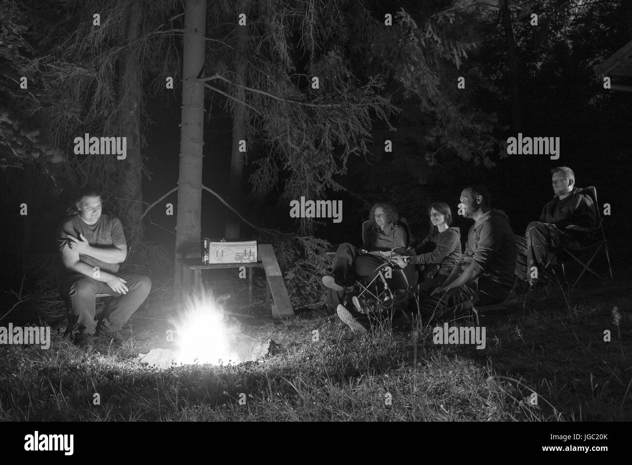 TUKLEKY, CZECH REPUBLIC - JULY 1, 2017: Group of adults around a fire pit in woods at night on July 1, 2017 in Tukleky village, Vysocina Region. Stock Photo