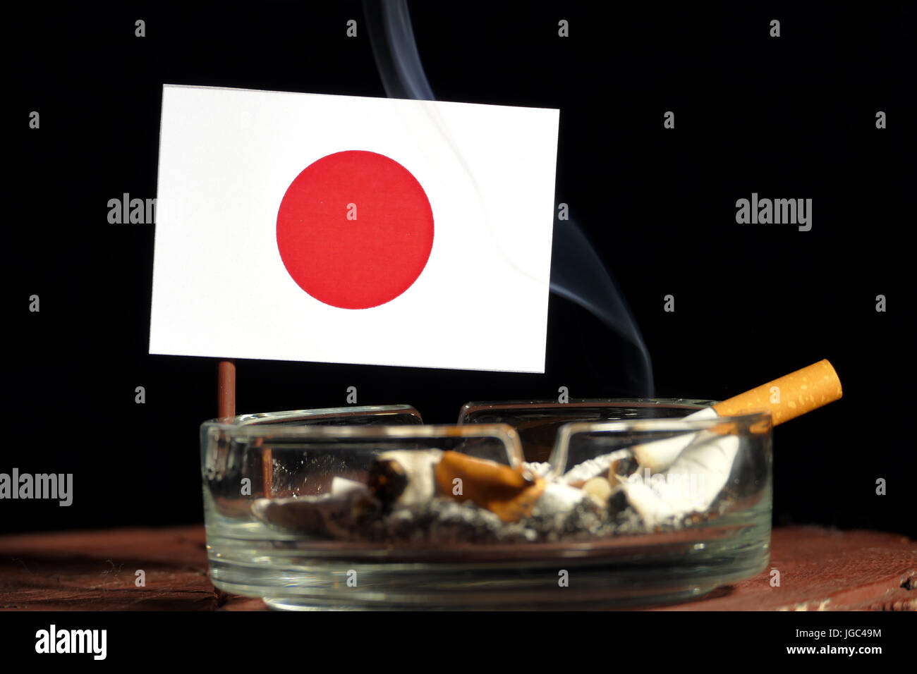 Japanese flag with burning cigarette in ashtray isolated on black background Stock Photo