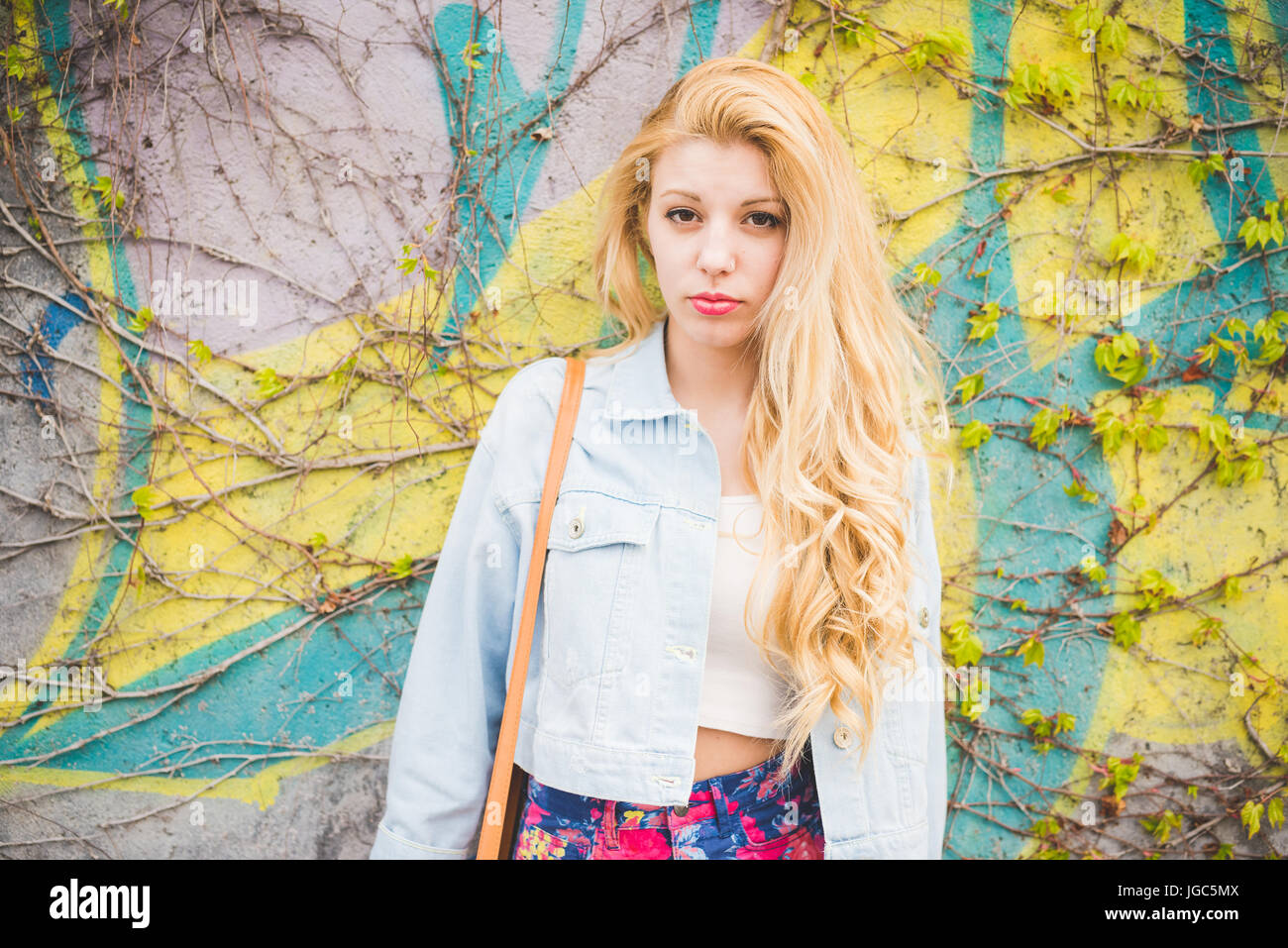 Young handsome blonde caucasian fashion girl posing leaning on a wall in the city suburbs Stock Photo