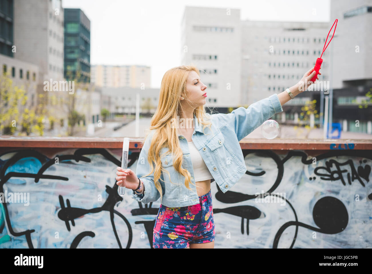 Young beautiful blonde caucasian girl playing with soap bubbles in the city suburbs - childhood, carefreeness concept Stock Photo