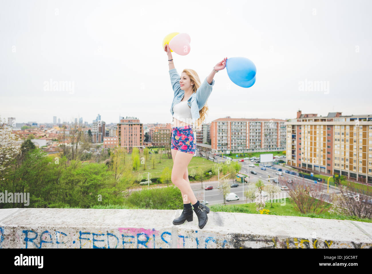 Young beautiful blonde caucasian girl playing with colorful balloons in te suburbs - childhood, carefreeness concept Stock Photo