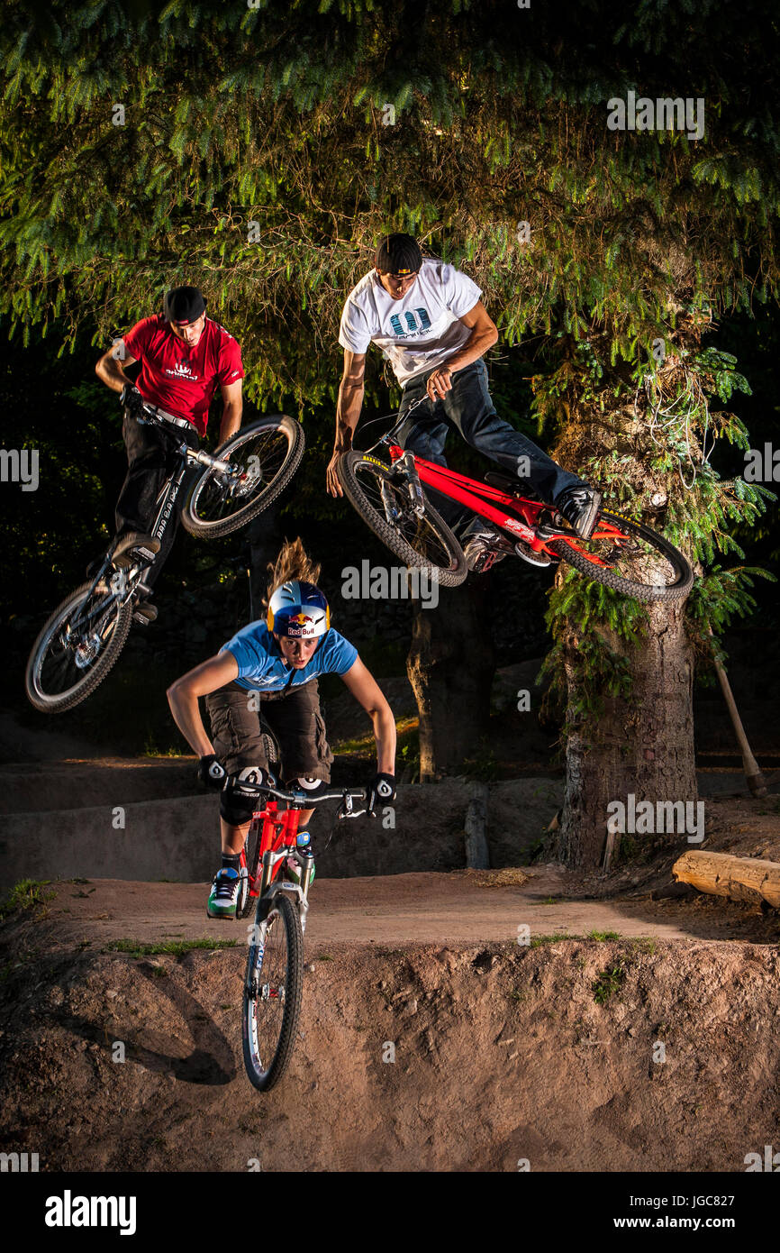 Professional mountain bikers and siblings - Gee, Dan and Rachel Atherton jumping their bikes on their backyard track. Stock Photo