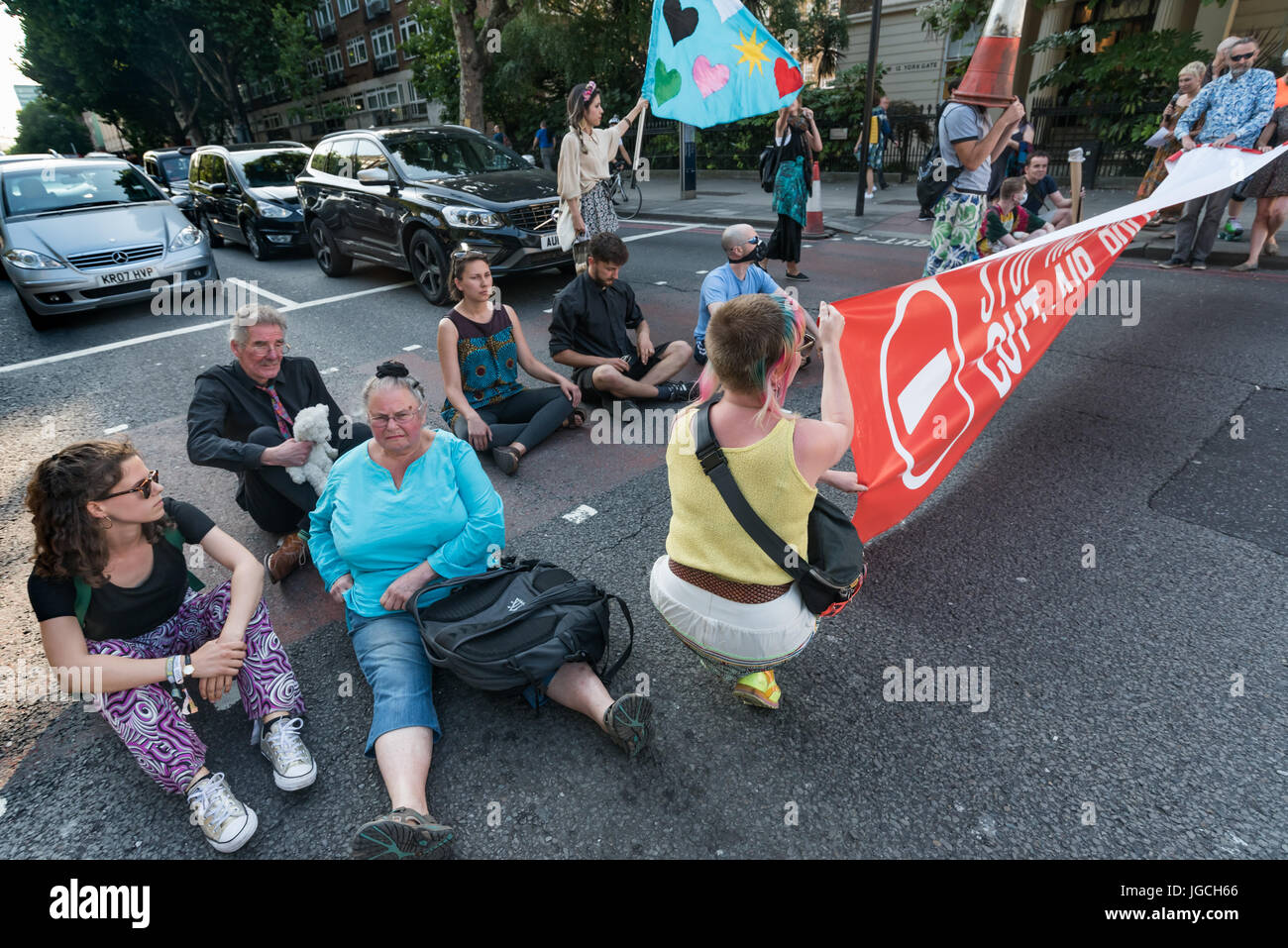London, UK. 5th July 2017. Rising Up campaigners sit on the road and get out the banner for their brief 'Staying' Alive' road-block disco on the east-bound carriageway of the Marylebone Road near Baker St to raise awareness about the terribly high pollution levels on London streets caused largely by traffic. They walked onto a pedestrian crossing, raised a banner, spoke briefly about the problem and then danced, holding up notices to the blocked motorists apologising  for the protest but pointing out that urgent action was needed and the protest would be short. One Volvo driver got out of his  Stock Photo