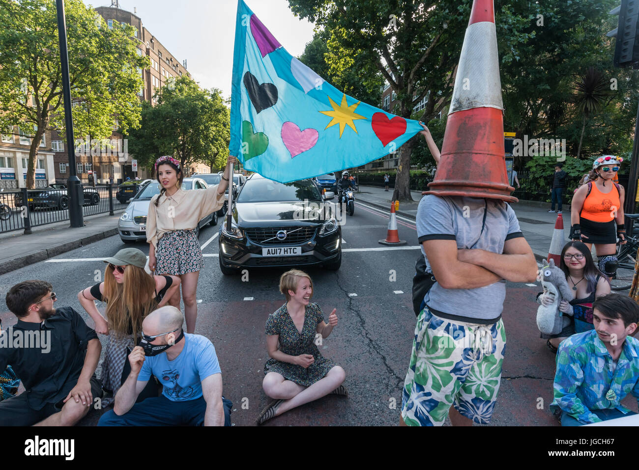 London, UK. 5th July 2017. Rising Up campaigners block the Marylebone Road for their brief road-block disco on the east-bound carriageway near Baker St to raise awareness about the terribly high pollution levels on London streets caused largely by traffic. They walked onto a pedestrian crossing, raised a banner, spoke briefly about the problem and then danced, holding up notices to the blocked motorists apologising  for the protest but pointing out that urgent action was needed and the protest would be short. One Volvo driver got out of his car and argued angrily, then made a half-hearted atte Stock Photo