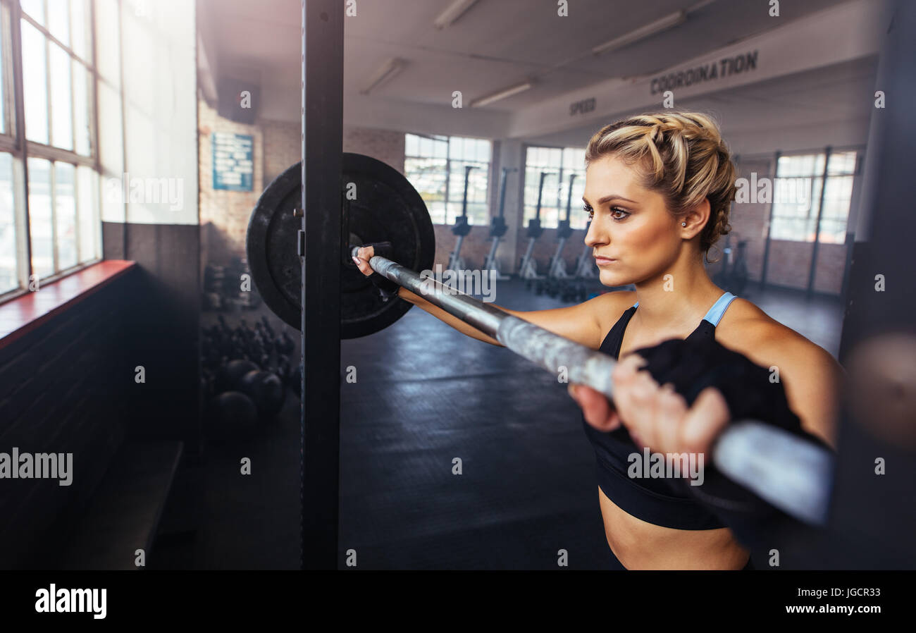 Female athlete doing exercise with weight bar at gym. Woman working out by lifting weights at gym. Stock Photo