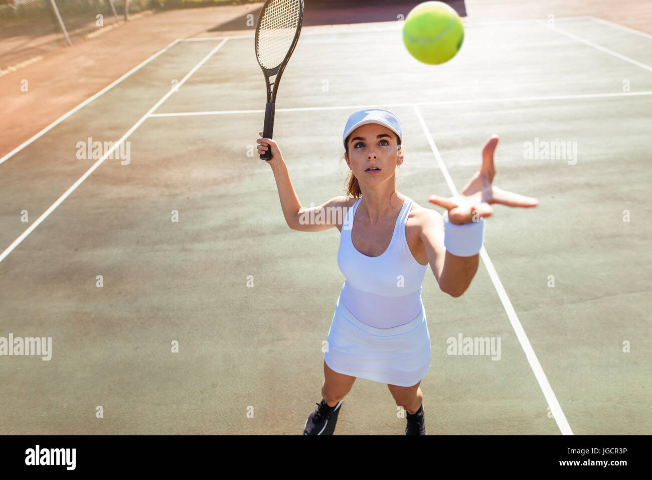 Beautiful young female tennis player serving the ball. Young woman in sportswear playing tennis match on court. Stock Photo