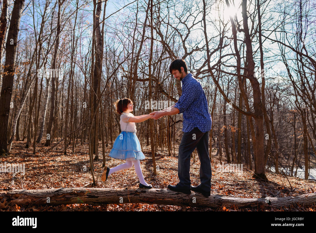 Father and daughter holding hands standing on a tree trunk in the ...