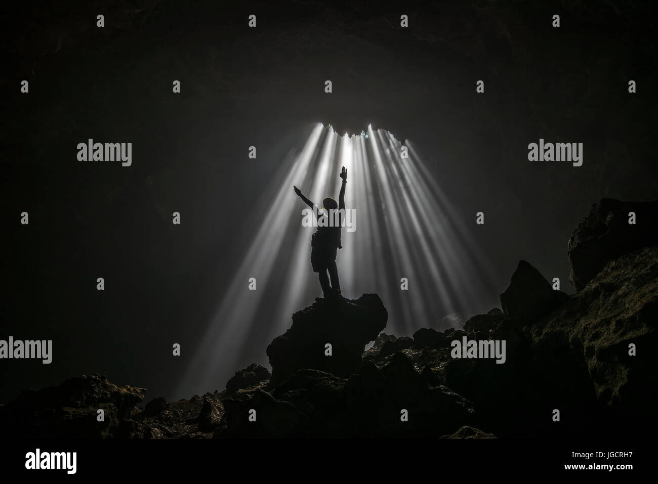 Silhouette of a man standing in a cave with arms raised, Jomblang, Central Java, Indonesia Stock Photo