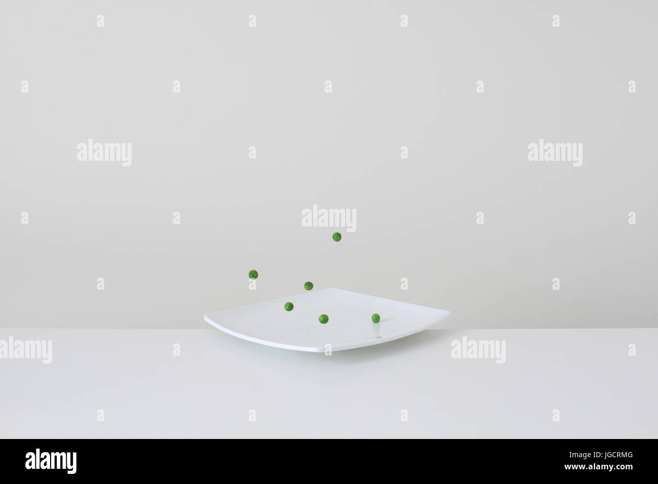 Conceptual green peas bouncing on plate Stock Photo