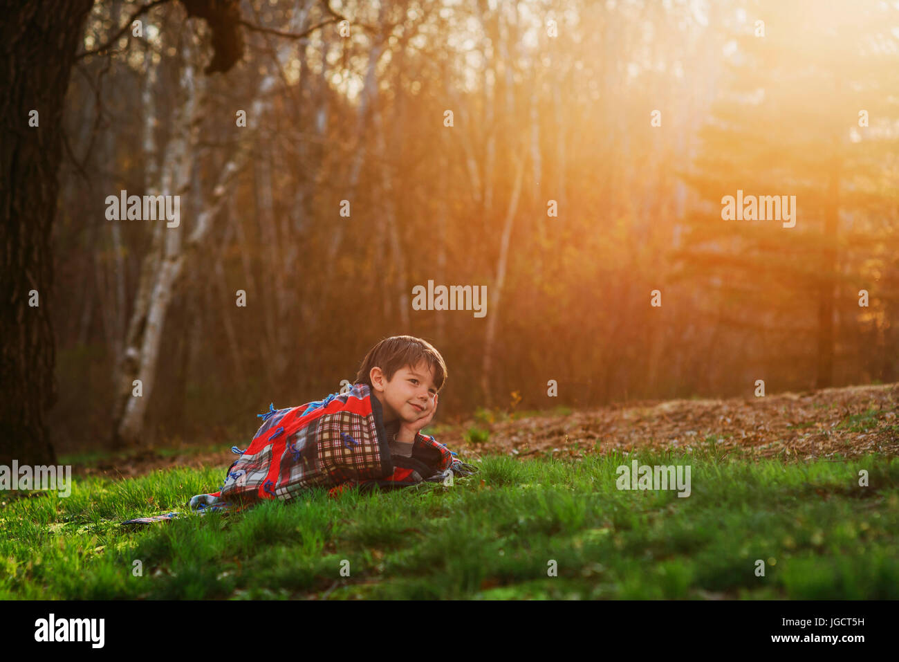 Boy lying on the grass wrapped in a blanket in the sun Stock Photo