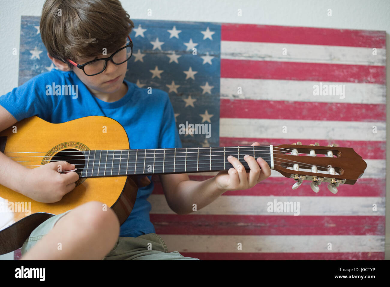 Boy sitting by an American flag playing the guitar Stock Photo