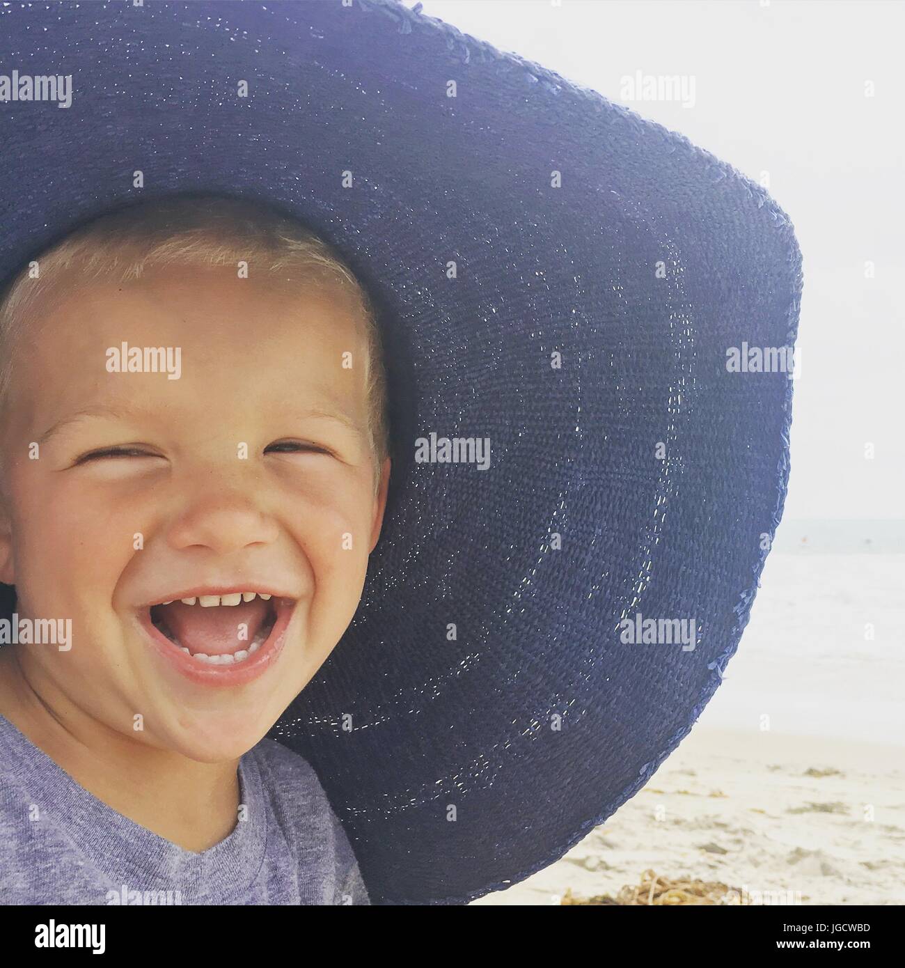 Boy wearing his mother's beach hat laughing Stock Photo