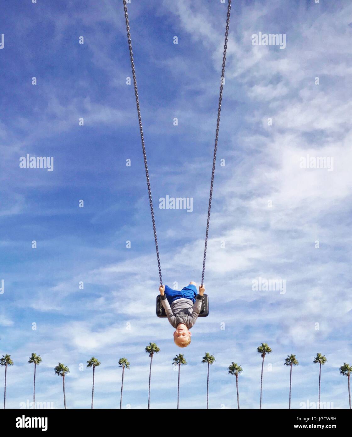 Boy swinging upside down on a swing over a row of palm trees, Orange County, California, United States Stock Photo