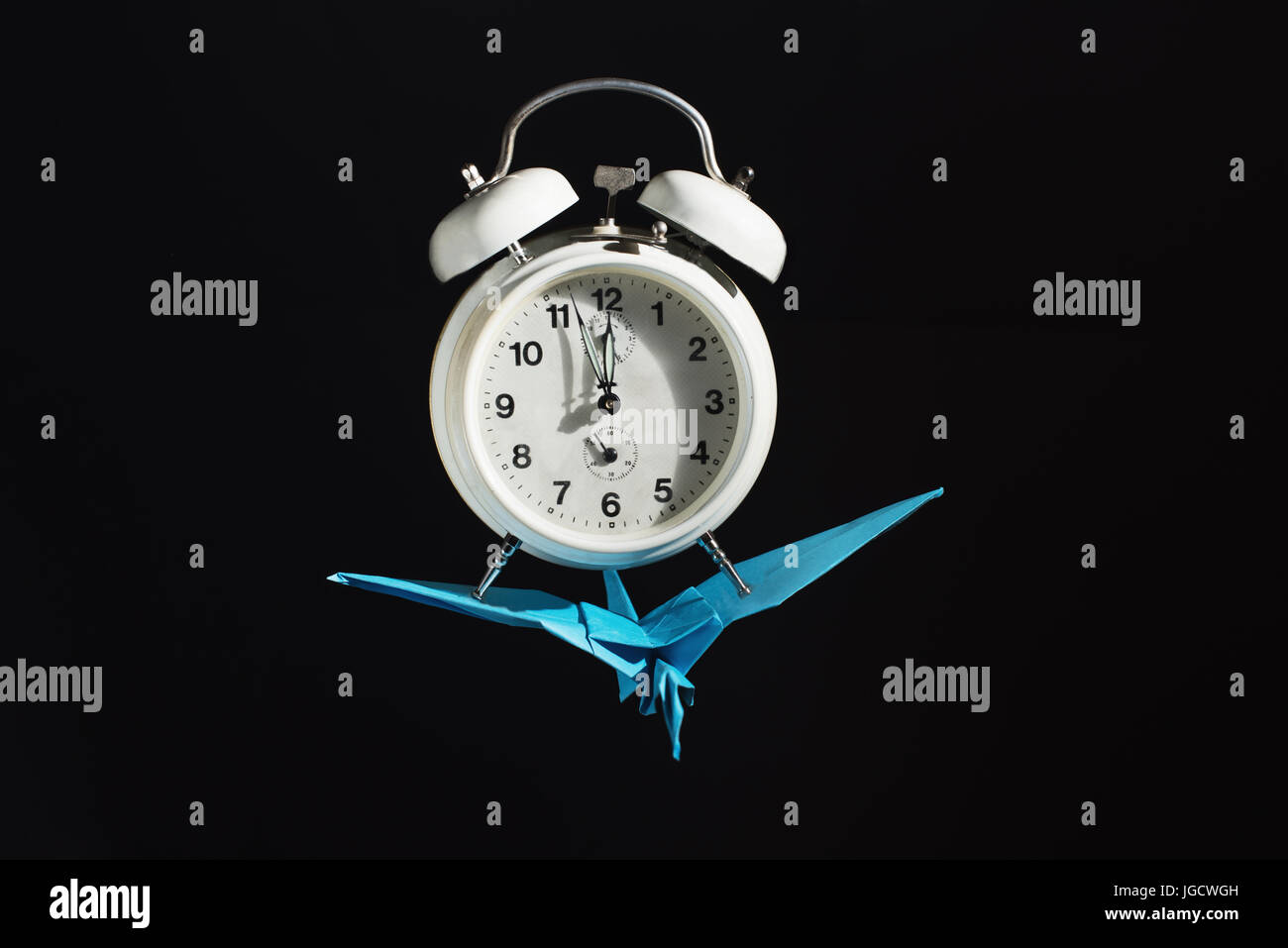 Origami bird flying with an alarm clock Stock Photo