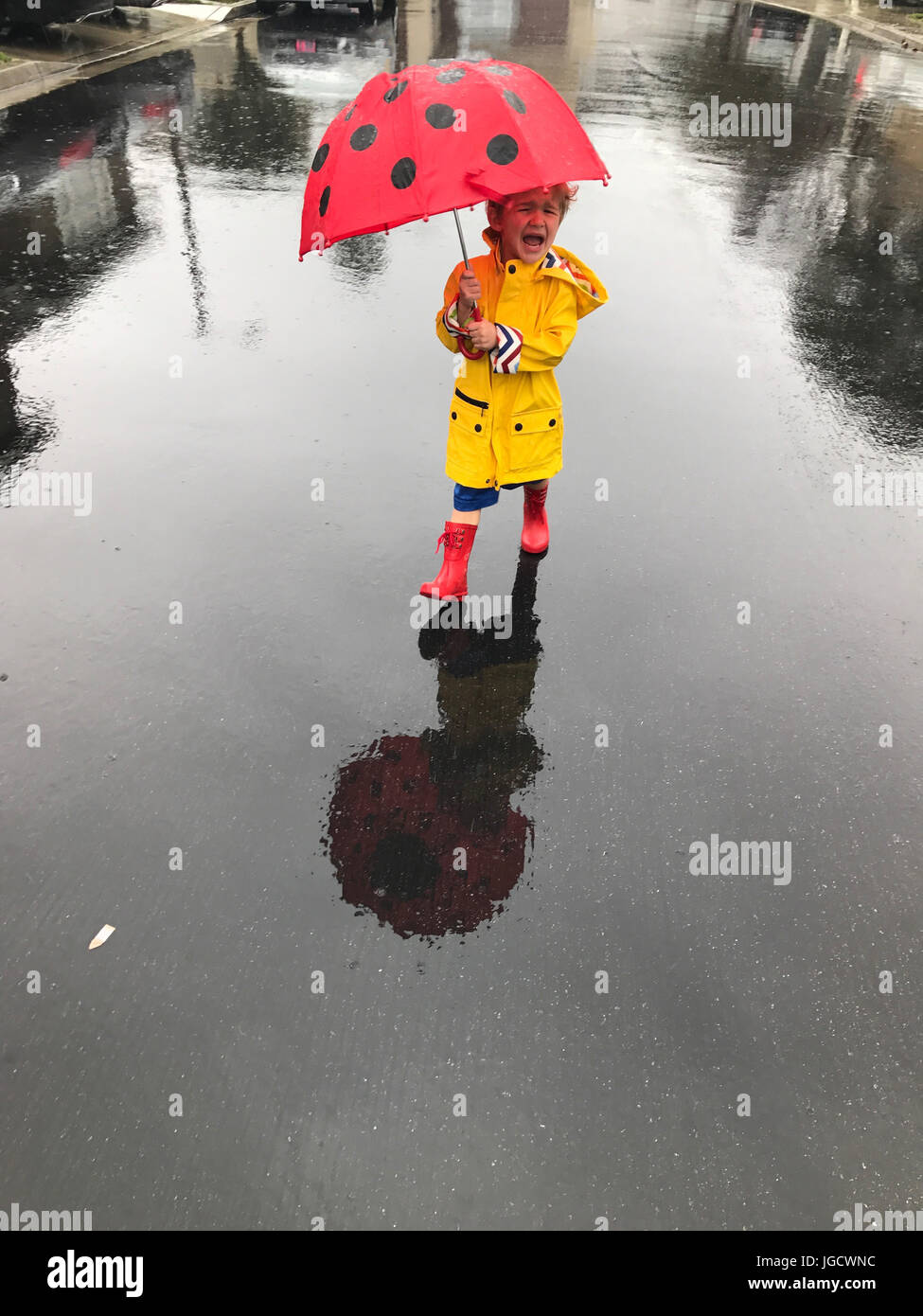 Crying boy wearing a raincoat and wellington boots standing in the rain with an umbrella, Orange County, California, America, USA Stock Photo