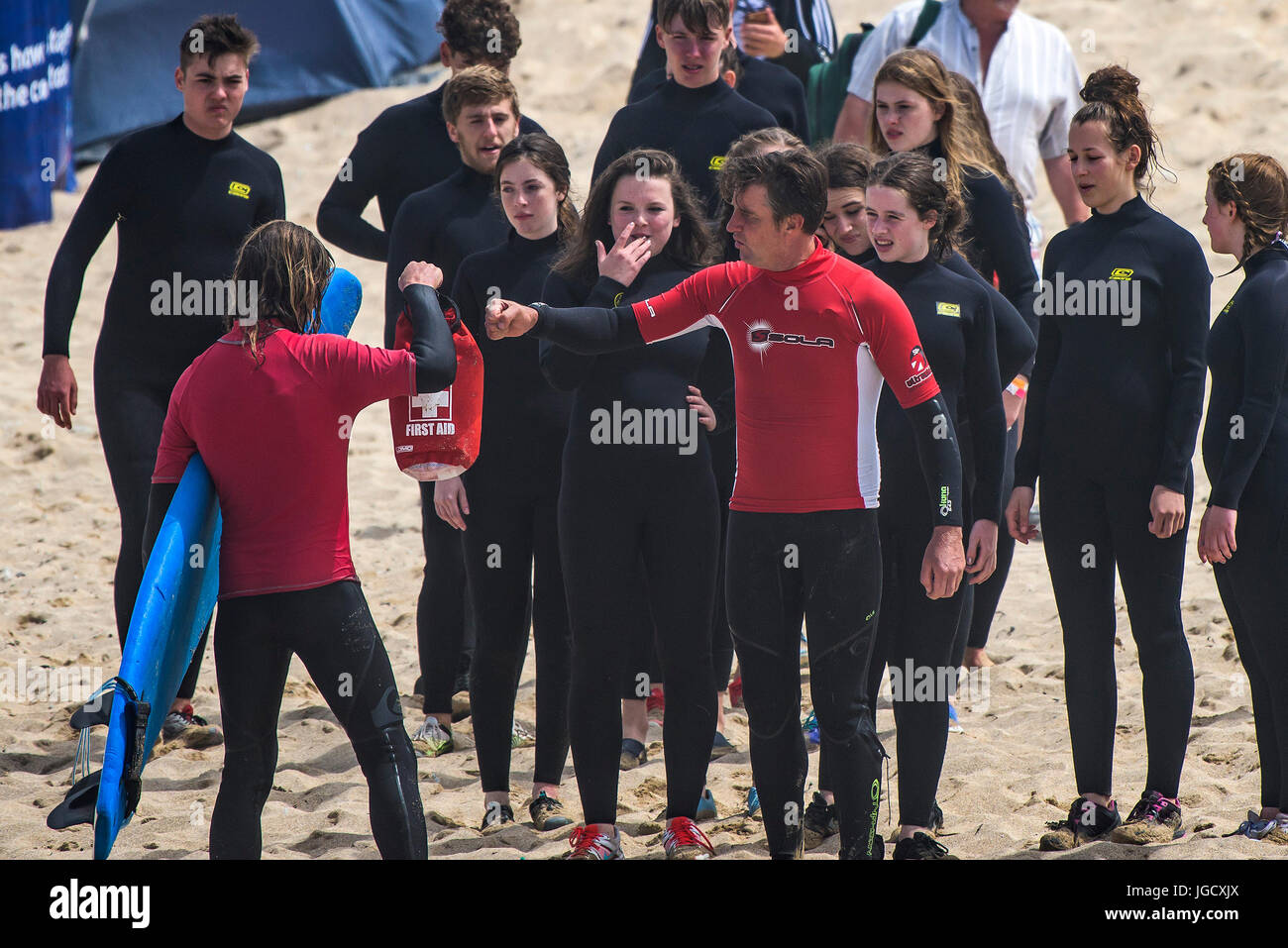 Surf school instructors greeting each other as a group of novices look on. Fistral Beach, Newquay, Cornwall. Stock Photo