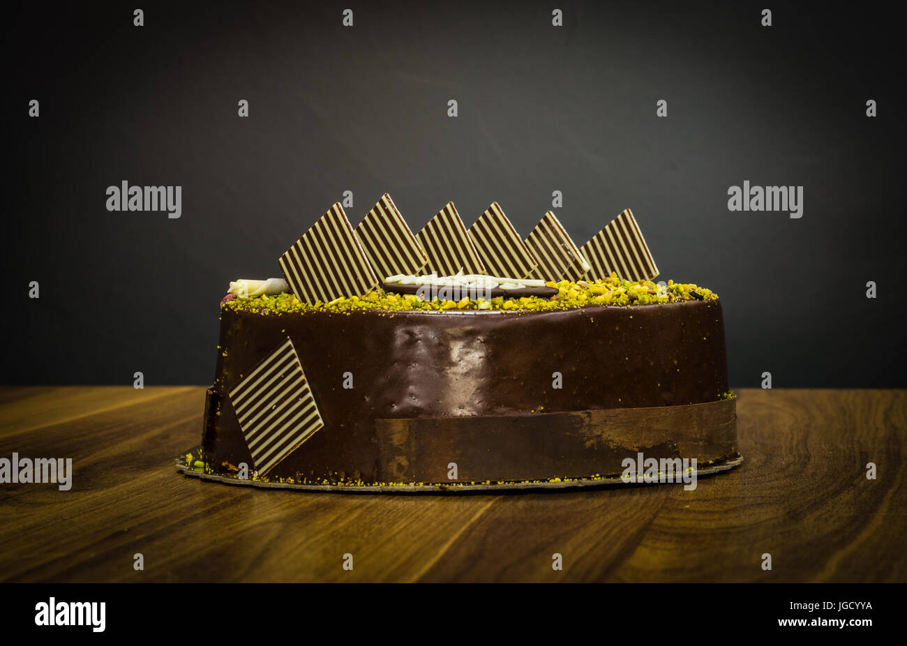 Delicious creamy whole dark chocolate cake with pistachio on topping on a dark background Stock Photo