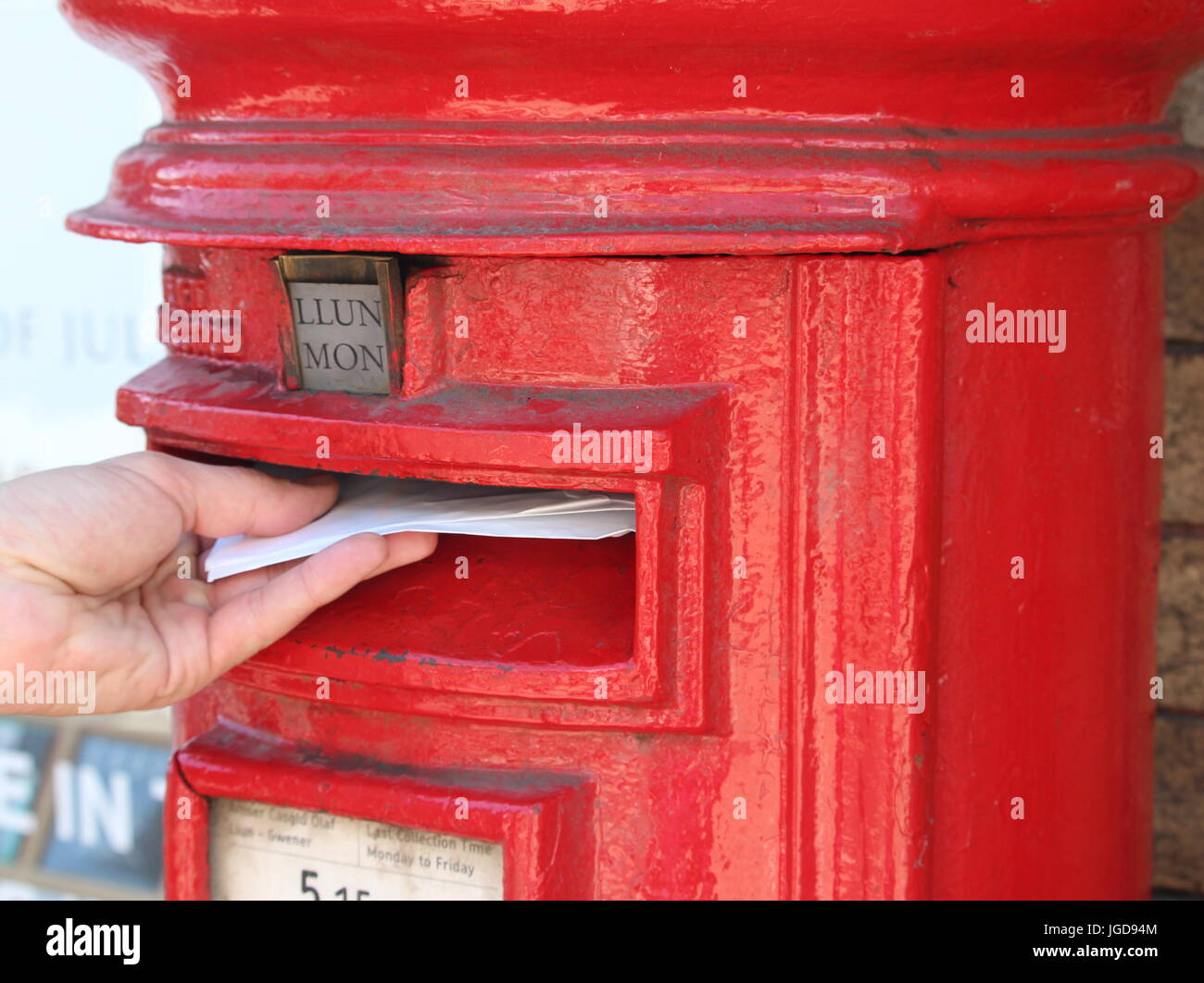 A male hand posting a letter into a letterbox which has bilingual (Welsh and English) signage. Abergavenny, UK. 2 July 2017 Stock Photo