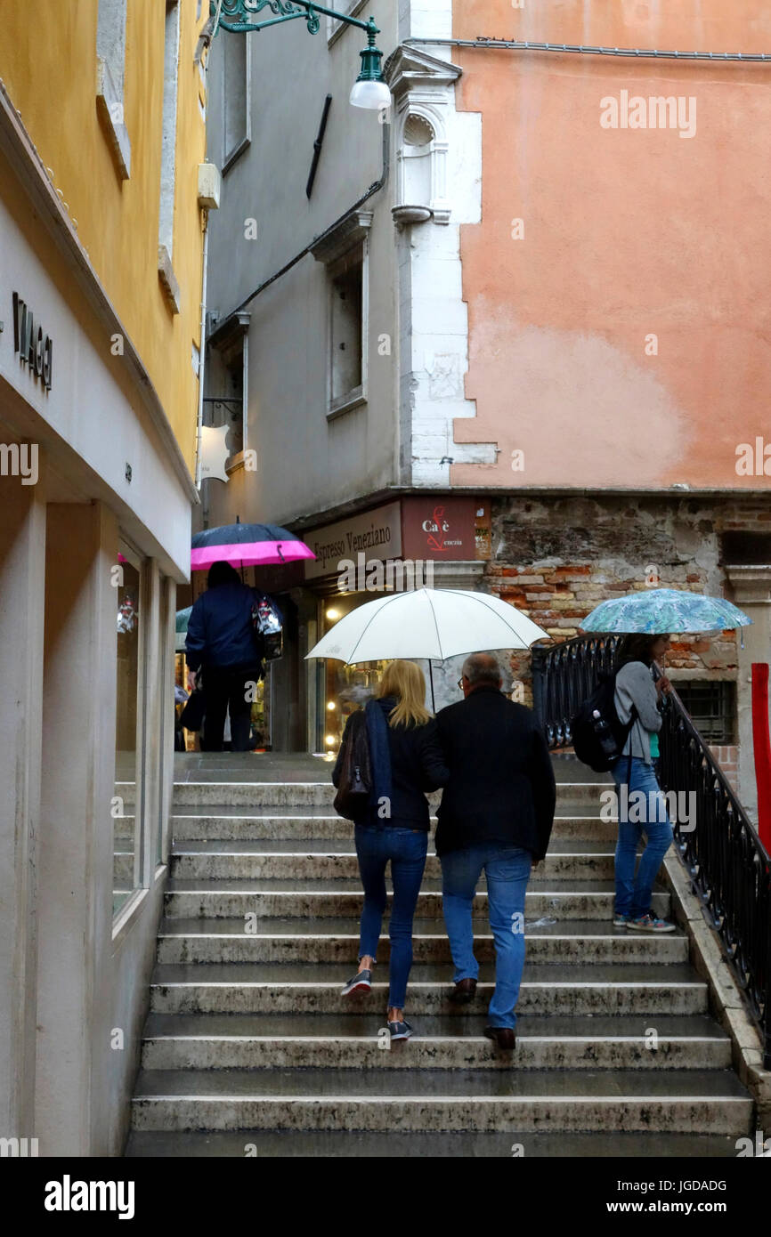 Pedestrians crossing over a canal via a small bridge in the rain, Venice,Venzia, Italy Stock Photo