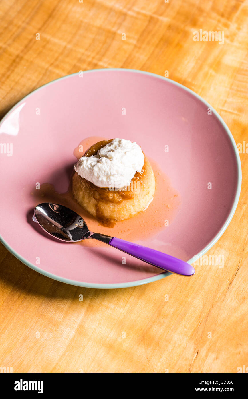 Flan - a sweet custard creme caramel with creme on top, on a pink plate over a wooden board. Stock Photo