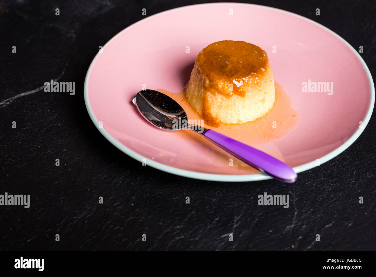 Flan - a sweet custard creme caramel with creme on top, on a pink plate over a wooden board. Stock Photo