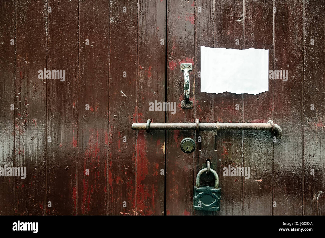 Old and dirty heavy wooden door with lock, bolt, handle and torn paper