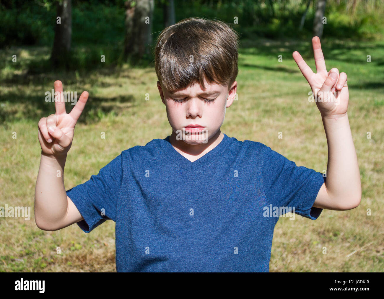 caucasian young boy making peace signs with his fingers outdoors Stock Photo