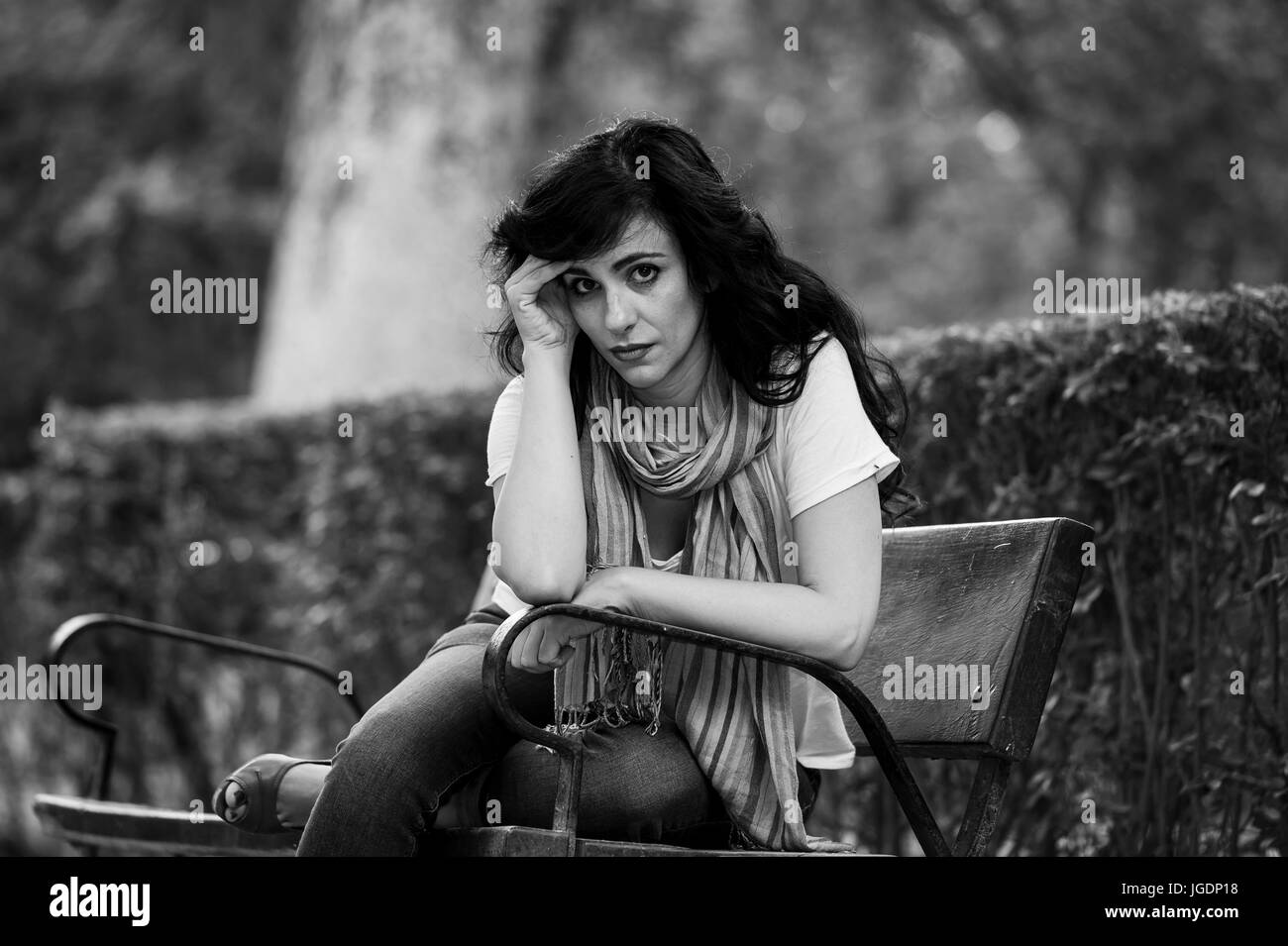 attractive beautiful latin woman sitting on a park bench feeling sad and depressed in a park outside in europe Stock Photo