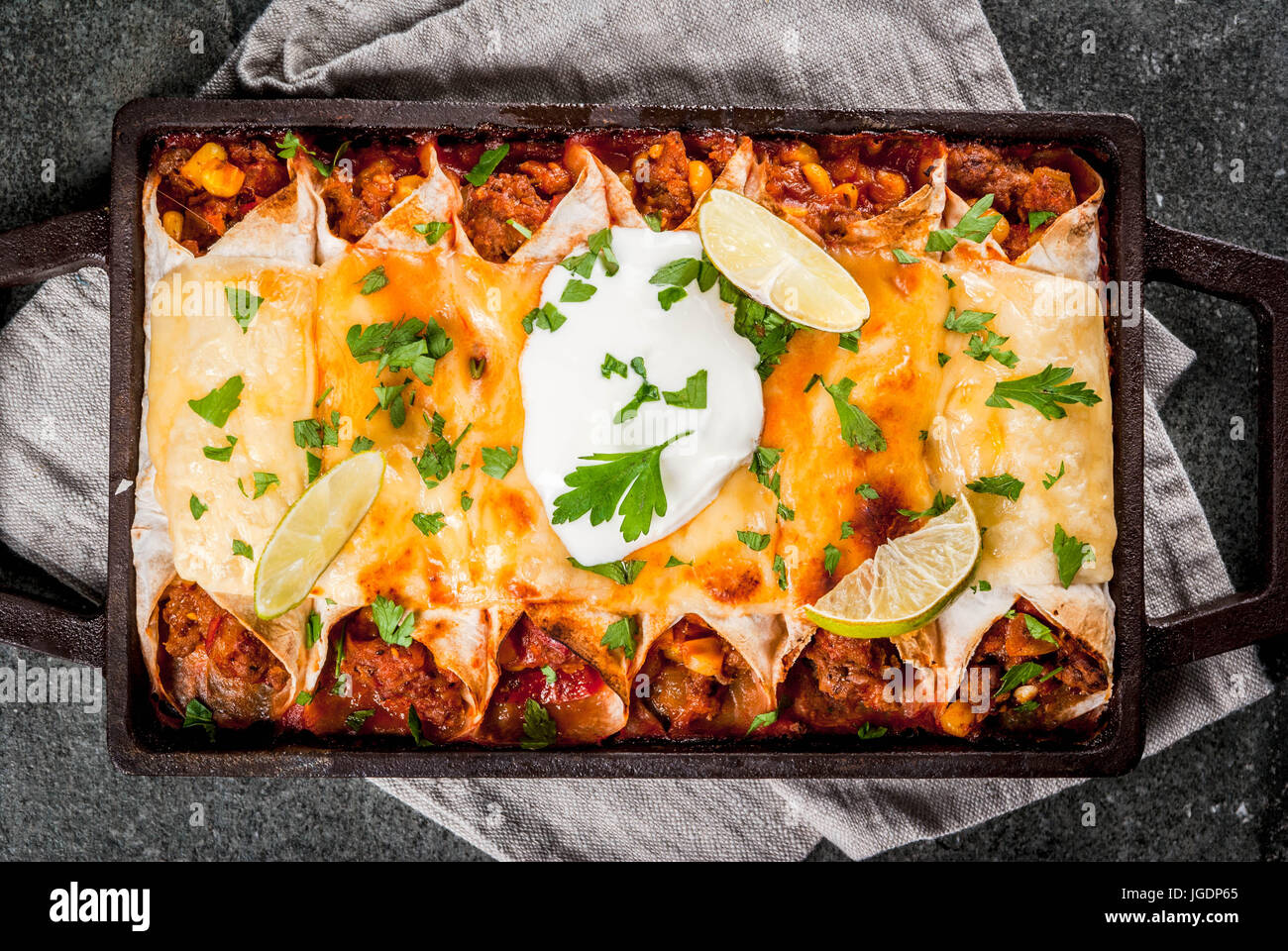 Mexican food. Cuisine of South America. Traditional dish of spicy beef enchiladas with corn, beans, tomato. On a baking tray, on a black stone backgro Stock Photo
