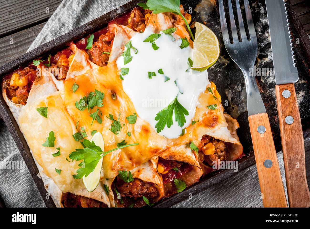 Mexican food. Cuisine of South America. Traditional dish of spicy beef enchiladas with corn, beans, tomato. On a baking tray, on old rustic wooden bac Stock Photo