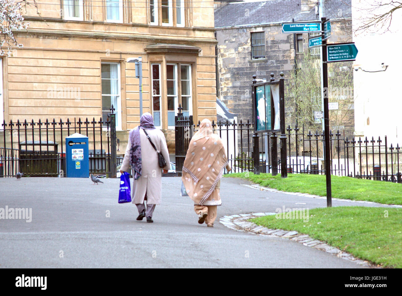 two hijab scarf wearing older ladies Muslim on British street at signpost with choices and exit gate Kelvingrove park Stock Photo