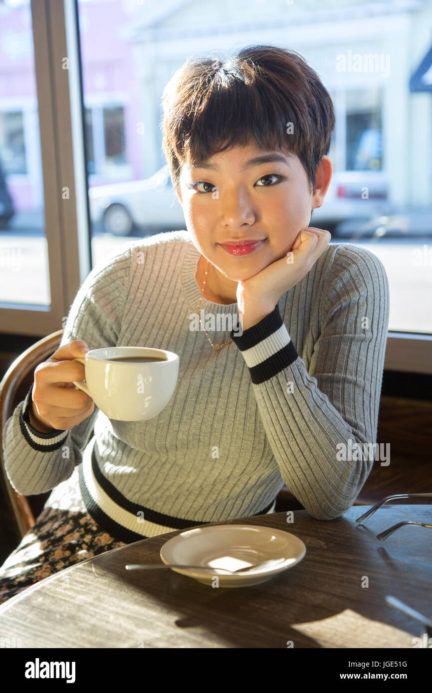 Serious Asian teenage girl drinking coffee in coffee shop Stock Photo