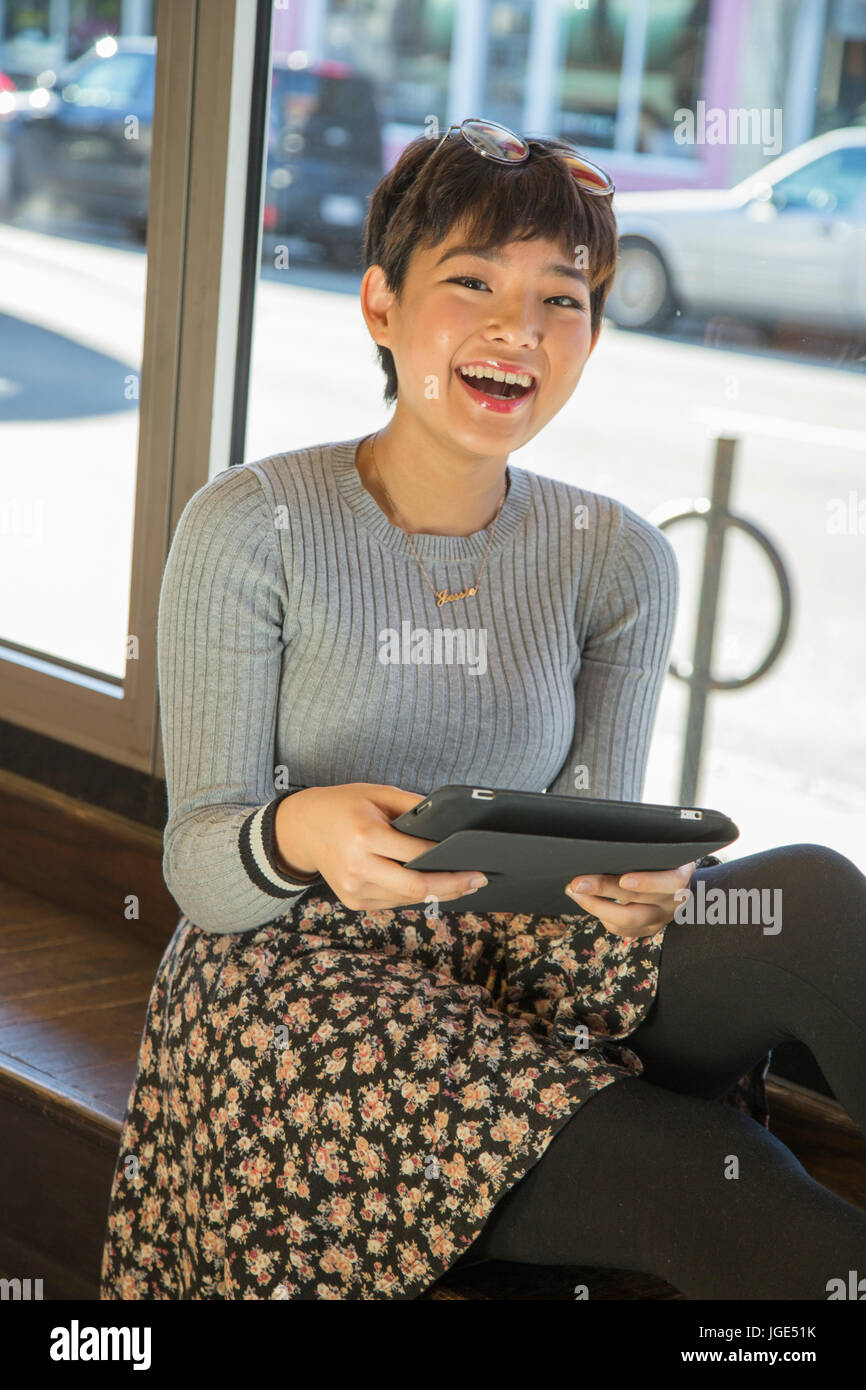 Asian teenage girl using digital tablet on window sill Stock Photo