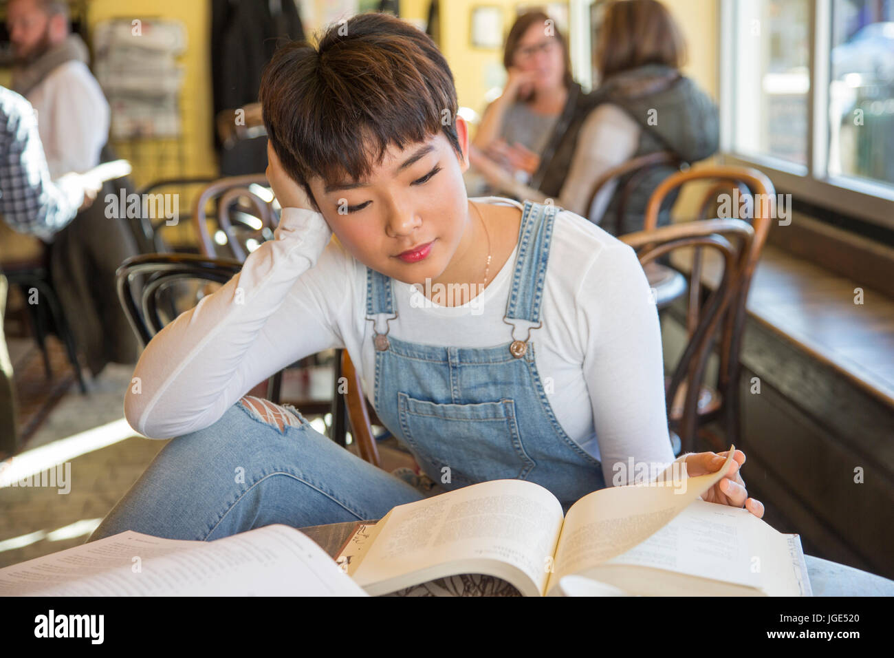 Asian teenage girl reading book in coffee shop Stock Photo