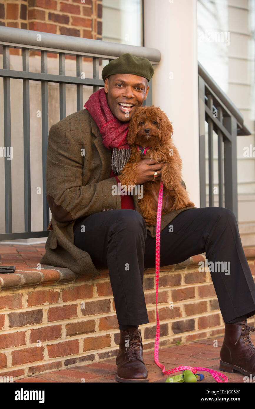 Portrait of African American man sitting on stoop holding dog Stock Photo