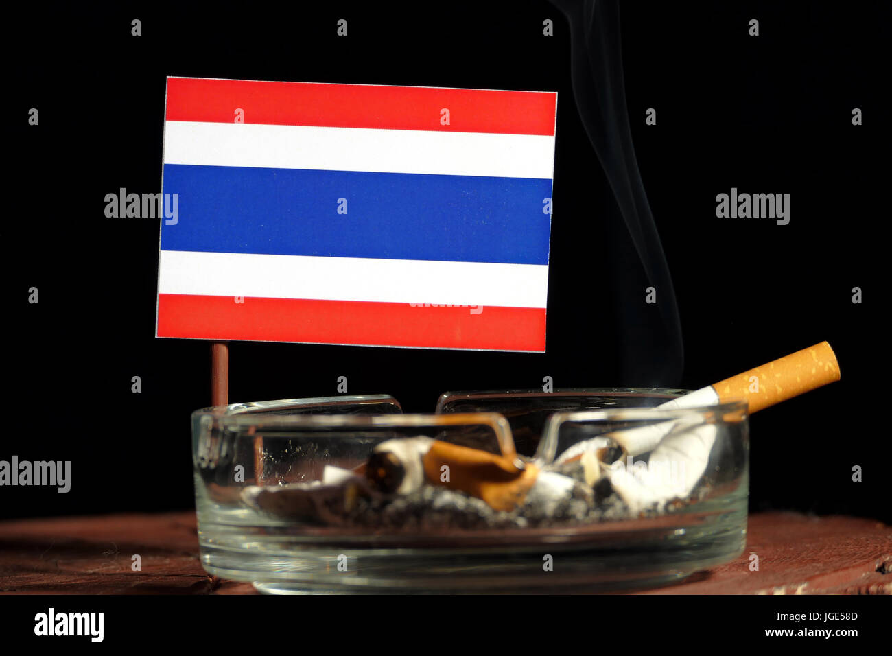 Thai flag with burning cigarette in ashtray isolated on black background Stock Photo